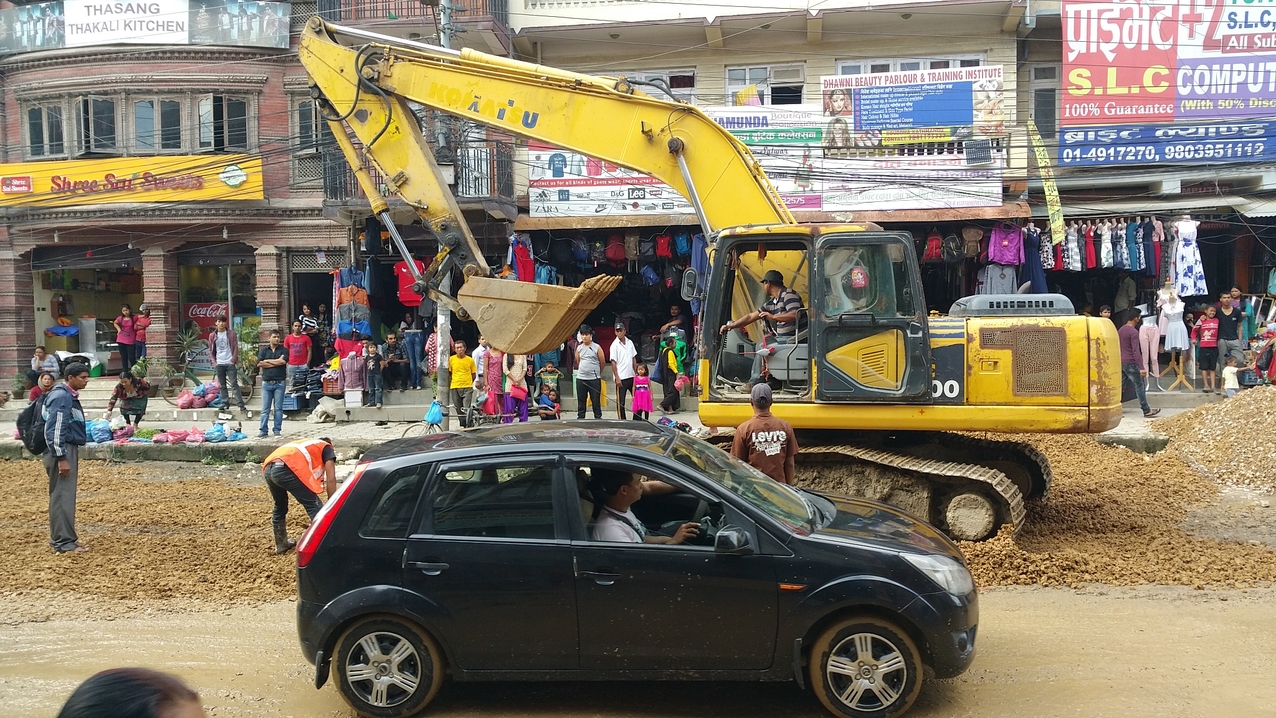 Nachdem Lastwagen mehrere Fuhren Schotter mitten im Verkehr abgeladen haben, beginnt die Verteilung.

